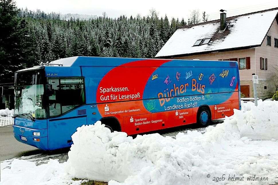 Bücherbus in blau und rot in einer Schneelandschaft.