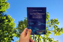 Blaues Buch vor blauem Himmel. Eine Hand hält das Buch in die Höhe.