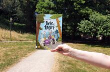 Eine Hand hält ein lustiges Buch vor einen Weg in einem Park.
