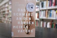 Buch steht hochkant auf einem Tisch vor einem Bücherregal.