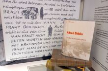 Buch auf Bücherstapel aufgestellt. Im Hintergrund sind Teile des Museumsbereichs zu Alfred Döblins Alexanderplatz zu sehen.