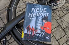 Buch liegt auf dem Vorderrad eines Fahrrades. Das Buchcover zeigt eine Person, die ein Fahrrad schiebt.