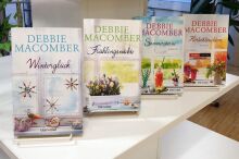 Vier Bücher von Debbie Macomber stehen in einer Reihe auf einem Tisch.