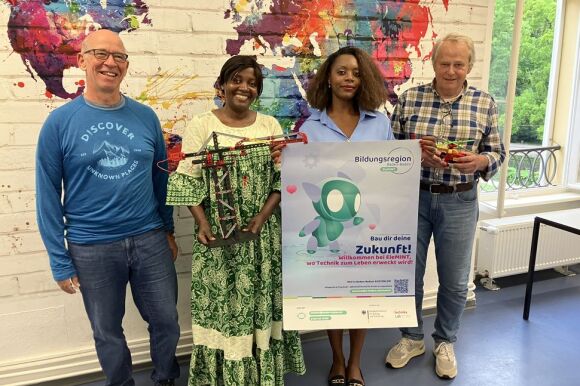 Vier Personen vor einer Weltkarte: eine hält das Plakat zur Bildungsregion Baden-Baden vor sich hin.