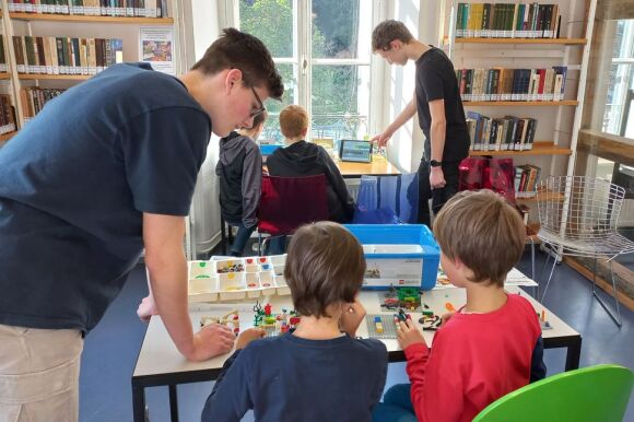 Lernatmosphäre mit LEGO. Zwei ältere Jungen helfen jüngeren Menschen bei Lego-Konstruktionen.