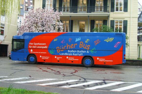Blauer Bücherbus vor der Stadtbibliothek mit blühendem Magnolienbaum