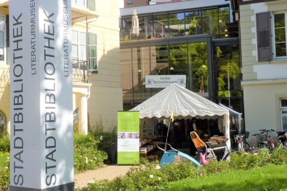 Eingang der Stadtbibliothek, davor ein großes Zelt des Bücherflohmarkts