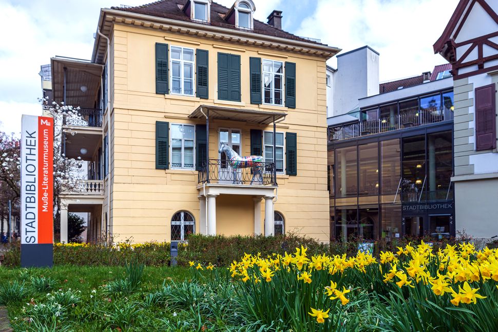 Gründerzeitvilla mit angebautem Gebäude aus Glas (Stadtbibliothek Baden-Baden). Osterglocken im Vordergrund.