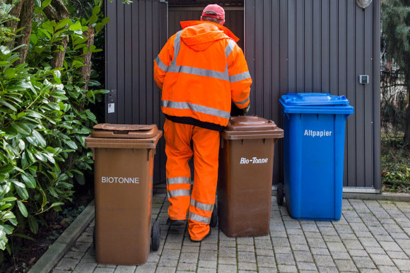 Mitarbeiter der Müllabfuhr neben zwei Bio- und einer Altpapiertonne