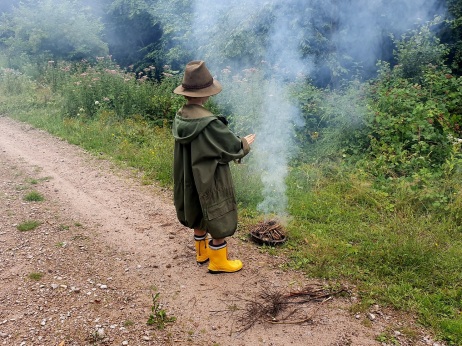 Ein Kind steht im Wald vor einem Feuer und hält die Hände über den Rauch. 