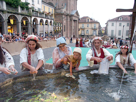 Frauen in historischer Kleidung waschen im Brunnen auf dem Kirchplatz in Moncalieri ihre Wäsche.