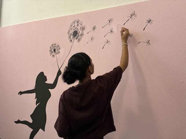 Ein Mädchen steht vor einer pinken Wand und malt.