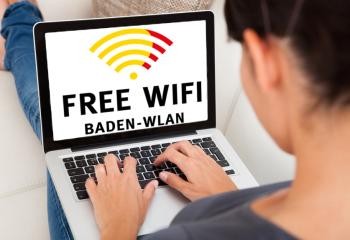 Baden-WLAN Frau sitzt vor Laptop, auf dem Bildschirm ein ganzformatifes Logo Free WiFi