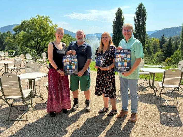 Vier Menschen stehen in einer Reihe im Rosenneuheitengarten auf dem Beutig und halten Plakate in ihren Händen.